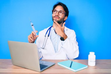 Klinikteki yakışıklı İspanyol doktor elinde şırıngayla ciddi bir yüz ifadesiyle eli çenesinde soruyu düşünüyor, kafa karıştırıcı bir fikir. 