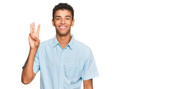 Genç, yakışıklı, Afro-Amerikalı, günlük kıyafetler giymiş, üç numaralı parmaklarıyla onu gösterirken, kendinden emin ve mutlu bir şekilde gülümsüyor.. 