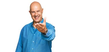 Orta yaşlı kel bir adam, günlük kıyafetler giyip gülümseyerek selamlaşma ve dostça tokalaşma teklif ediyor. başarılı iş. 