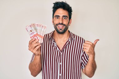 Yakışıklı, sakallı, Kolombiya pezosu tutan ve ağzı açık gülümseyen bir İspanyol. 