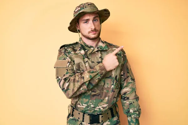 広告を示す側に手指で指しているカモフラージュ軍の制服を着て若い白人男性 深刻かつ穏やかな顔 — ストック写真