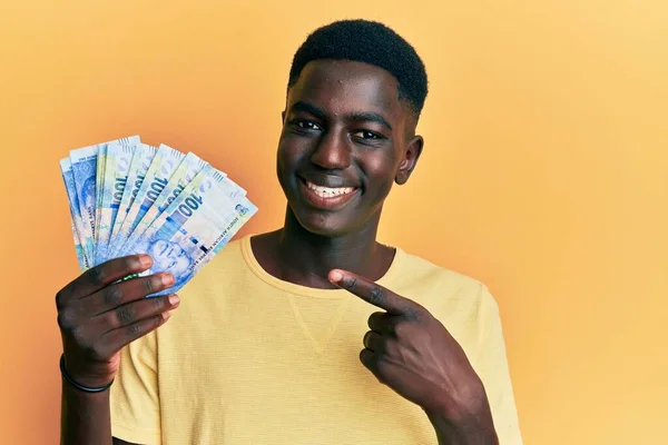 Молодий Афроамериканець Тримає Південноафриканські Банкноти Усміхається Показуючи Пальцем Рукою — стокове фото