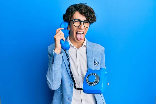 西班牙裔年轻人在老式电话里说话时 带着滑稽的表情 伸出舌头 高兴极了 — 图库照片