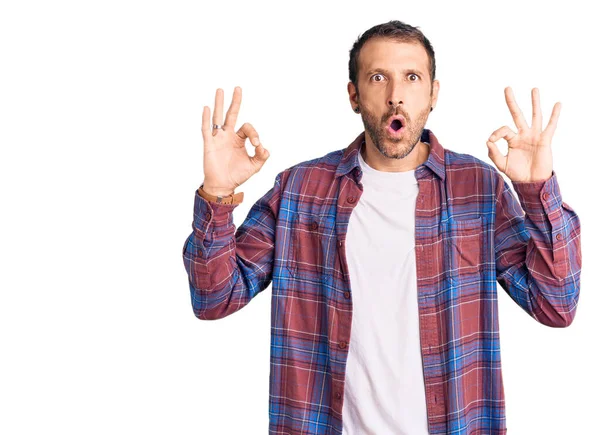 Gündelik kıyafetler giyen genç yakışıklı adam şaşırmış ve şok olmuş görünüyor. Tamam sembolünü parmaklarıyla yapıyor. çılgın ifade 