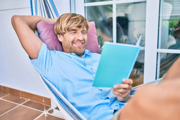 Orta yaşlı yakışıklı bir adam evinin terasında bir hamakta uzanıp kitap okuyor.