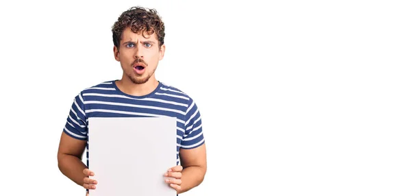 Young Handsome Man Curly Hair Holding Blank Empty Banner Scared — Stock Photo, Image