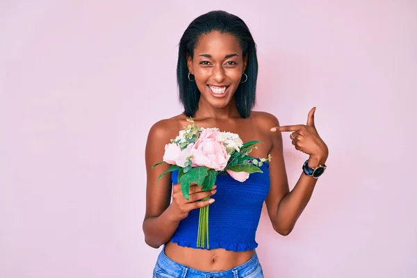 Νεαρή Αφροαμερικανή Που Κρατάει Λουλούδια Δείχνοντας Τον Εαυτό Της Χαμογελώντας — Φωτογραφία Αρχείου