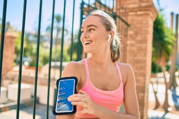 Genç sarışın sporcu, şehirde egzersiz yaparken kulaklık takıyor.