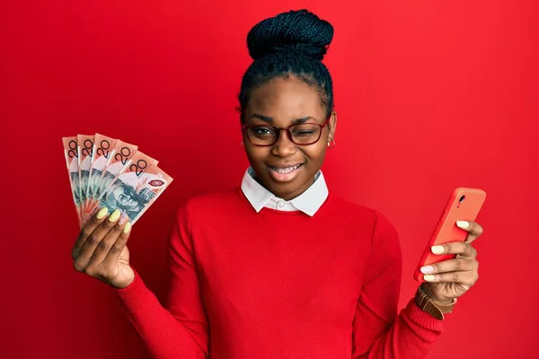 Joven Mujer Afroamericana Usando Smartphone Sosteniendo Billetes Dólar Australiano Guiñando —  Fotos de Stock