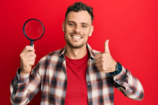 Joven Hombre Hispano Sosteniendo Lupa Buscando Mancha Ropa Sonriendo Feliz —  Fotos de Stock