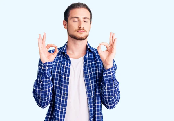 Gündelik kıyafetler giyen yakışıklı beyaz adam rahatla ve parmaklarıyla meditasyon hareketi yaparken gözleri kapalı gülümse. yoga konsepti. 