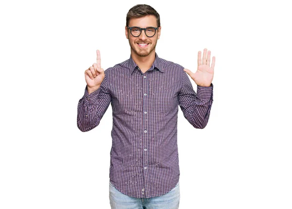 Yakışıklı beyaz adam, günlük kıyafetler ve gözlük takıyor. Altıncı parmaklarını gösterip işaret ediyor. Kendinden emin ve mutlu gülümsüyor.. 