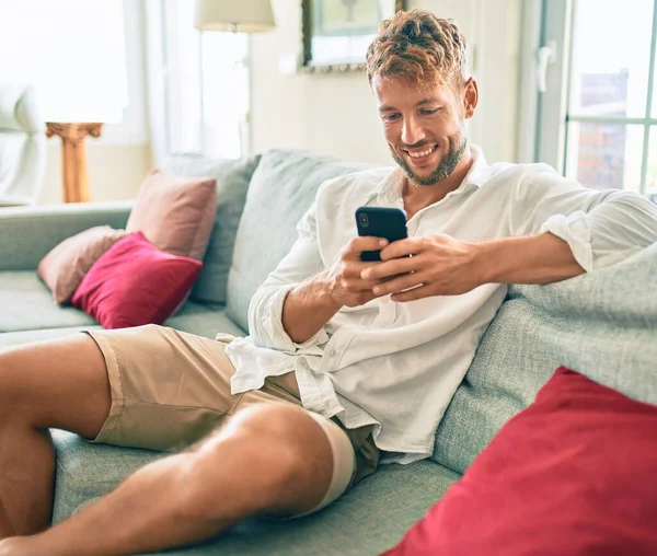 Yakışıklı Beyaz Adam Mutlu Gülümsüyor Evdeki Kanepede Otururken Akıllı Telefon — Stok fotoğraf