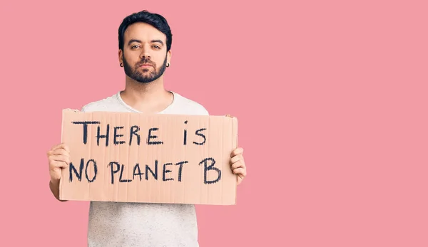 Young hispanic man holding there is no planet b banner thinking attitude and sober expression looking self confident