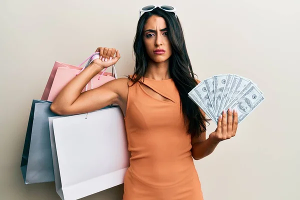 Schöne Hispanische Frau Mit Einkaufstaschen Und Dollars Skeptisch Und Nervös — Stockfoto