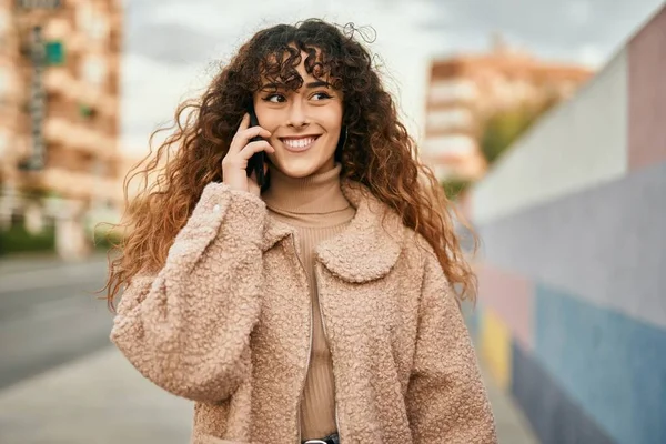 Genç İspanyol kadın gülümsüyor. Şehirdeki akıllı telefondan konuşuyor.