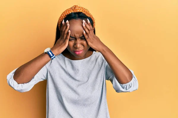痛みや片頭痛のために絶望的な頭痛やストレスに苦しんで黄色の背景にカジュアルな服を着て若いアフリカの女性 手を頭に — ストック写真