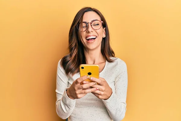 Młoda Brunetka Kobieta Pomocą Smartfona Żółtym Tle Uśmiecha Się Śmieje — Zdjęcie stockowe