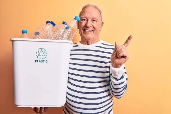 サイドに手と指で幸せなポインティング笑顔のペットボトルでいっぱいの老ハンサムな白髪の男のリサイクル — ストック写真