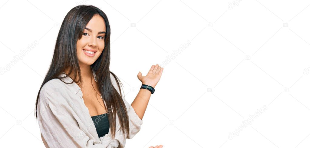 Young beautiful hispanic girl wearing casual clothes inviting to enter smiling natural with open hand 