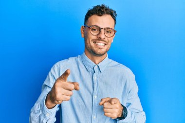 Gündelik kıyafetler giyen ve gözlüklü genç İspanyol adam mutlu ve komik yüzlü parmaklarını kameraya doğrultuyor. iyi enerji ve titreşimler. 