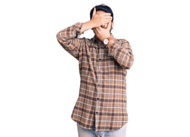 Gündelik kıyafetler giyen genç İspanyol adam gözlerini ve ağzını elleriyle kapatıyor, şaşırmış ve şok olmuş. duygu gizleme 