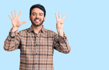 Gündelik kıyafetler giyen genç İspanyol adam sekiz numarayı gösterip işaret ederken kendinden emin ve mutlu bir şekilde gülümsüyor.. 
