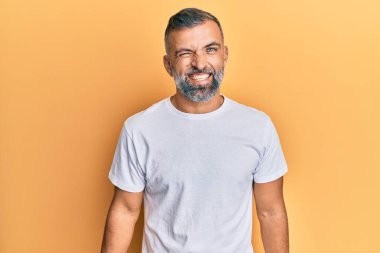 Orta yaşlı beyaz tişört giyen yakışıklı bir adam kameraya seksi bir ifadeyle bakıyor, neşeli ve mutlu bir yüzle.. 