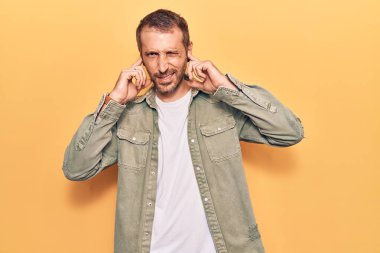 Gürültülü müzik sesi için kulaklarını parmaklarıyla kapatan sıradan kıyafetler giyen genç yakışıklı bir adam. sağır kavramı. 