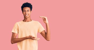 Genç Afrikalı Amerikalı sıradan kıyafetler giyen, elleri büyük ve büyük boy işareti gösteren, ölçü sembolü olan bir adam. Kameraya bakıp gülümsüyor. ölçüm kavramı. 