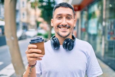Kulaklık takan genç İspanyol adam şehir caddesinde kahve içiyor..