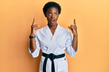 Karate kimonosu ve siyah kuşak giyen genç Afrikalı Amerikalı kız şaşırmış ve şaşırmış bir şekilde yukarı bakıyor ve parmaklarını gösterip kollarını kaldırıyordu.. 