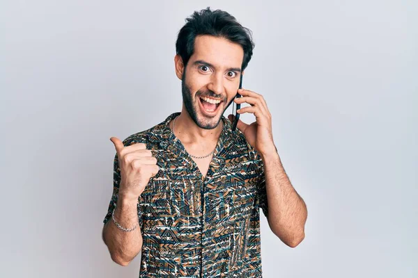 Joven Hispano Conversando Hablando Smartphone Apuntando Con Pulgar Hacia Lado — Foto de Stock