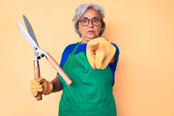Starsza Latynoska Kobieta Fartuchu Ogrodnika Rękawiczkach Trzymająca Nożyce Wskazujące Palcem — Zdjęcie stockowe