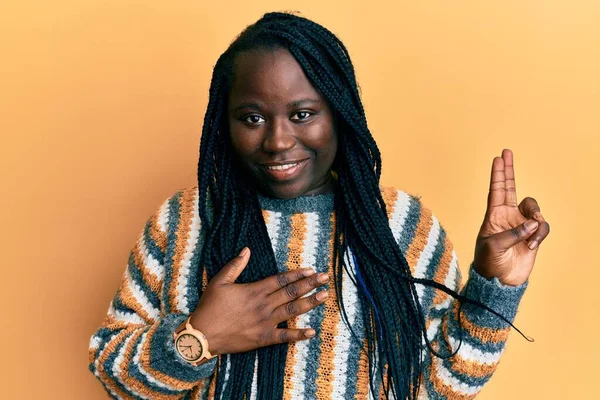 Young black woman with braids wearing casual winter sweater smiling swearing with hand on chest and fingers up, making a loyalty promise oath