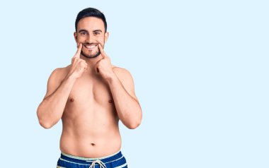 Mayo giyen, ağzı açık gülümseyen, parmakları işaret eden ve zorla gülümseyen genç yakışıklı bir adam. 