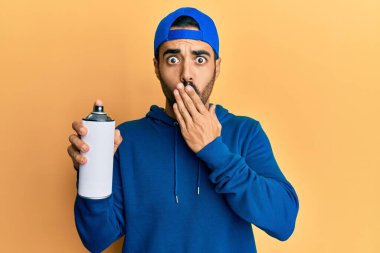Süveter giyen genç İspanyol adam elinde grafiti spreyi tutarak ağzını eliyle kapadı, şok oldu ve hata yapmaktan korktu. şaşırmış ifade 