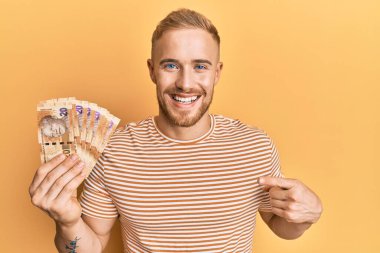 Güney Afrika 'da elinde 20 rand banknot tutan beyaz bir adam mutlu bir şekilde elini ve parmağını göstererek gülümsüyor. 