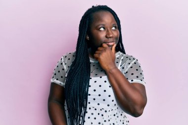 Saçları örgülü, elleri çenesinde gündelik kıyafetler giyen, soru soran, düşünceli bir genç siyahi kadın. Düşünceli bir yüzle gülümsüyor. şüphe kavramı. 