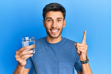 Genç yakışıklı bir adam bir fikir ya da soruyla gülümseyen bir bardak su içiyor. 