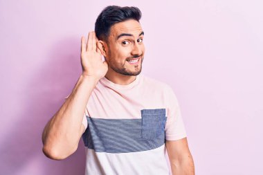 Sakallı, sıradan tişörtlü, pembe arka planda dikilen, kulağına fısıldayan, dedikoduları ve dedikoduları dinleyen genç yakışıklı bir adam. Sağırlık kavramı.