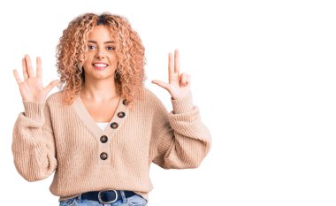 Kış kazağı giyen, kıvırcık saçlı genç sarışın kadın sekiz numaralı parmaklarıyla kendini beğenmiş ve mutlu gülümserken kendini gösteriyor.. 