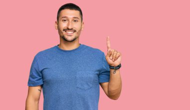 Dövmeleri olan yakışıklı bir adam. Günlük giysiler giyiyor. Bir numarayı gösteriyor ve gülümsüyor.. 