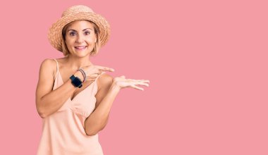 Yazlık şapkalı genç sarışın kadın kameraya hayret ediyor ve gülümsüyor.. 