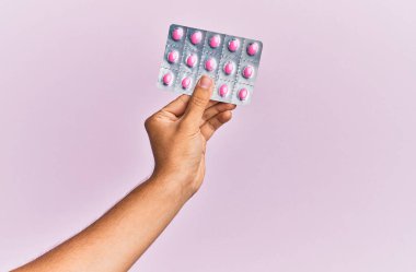 İzole edilmiş pembe arka planda hapları tutan İspanyol bir adam..