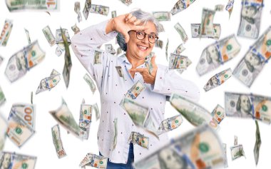 Gri saçlı, sıradan iş kıyafetleri giyen ve gözlüklü, gülümseyen, elleri ve parmakları mutlu yüzlü yaşlı bir kadın. yaratıcılık ve fotoğrafçılık kavramı.