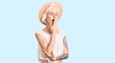 Yazlık şapka takan genç sarışın kadın, ağız ve ağızla esnemekten sıkılmış. Huzursuz ve uykulu.. 