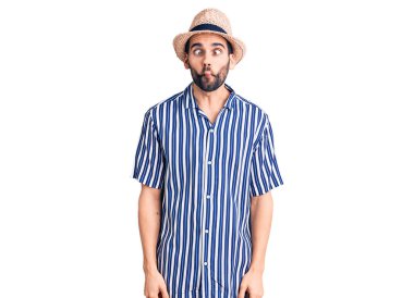 Sakallı, yaz şapkalı ve çizgili gömlekli genç yakışıklı adam dudaklı balık suratı yapıyor, çılgınca ve komik bir jest. Komik ifade. 