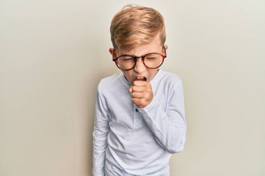 Günlük kıyafetler ve gözlük takan küçük beyaz çocuk kendini iyi hissetmiyor ve soğuk algınlığı veya bronşitin belirtisi olarak öksürüyor. sağlık hizmeti kavramı. 