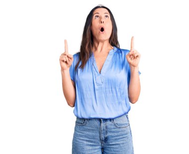 Genç, güzel, esmer, sıradan tişörtler giyen bir kadın şaşırmış ve şaşırmış bir şekilde yukarı bakıyor, parmaklarıyla işaret ediyor ve kollarını kaldırıyordu.. 